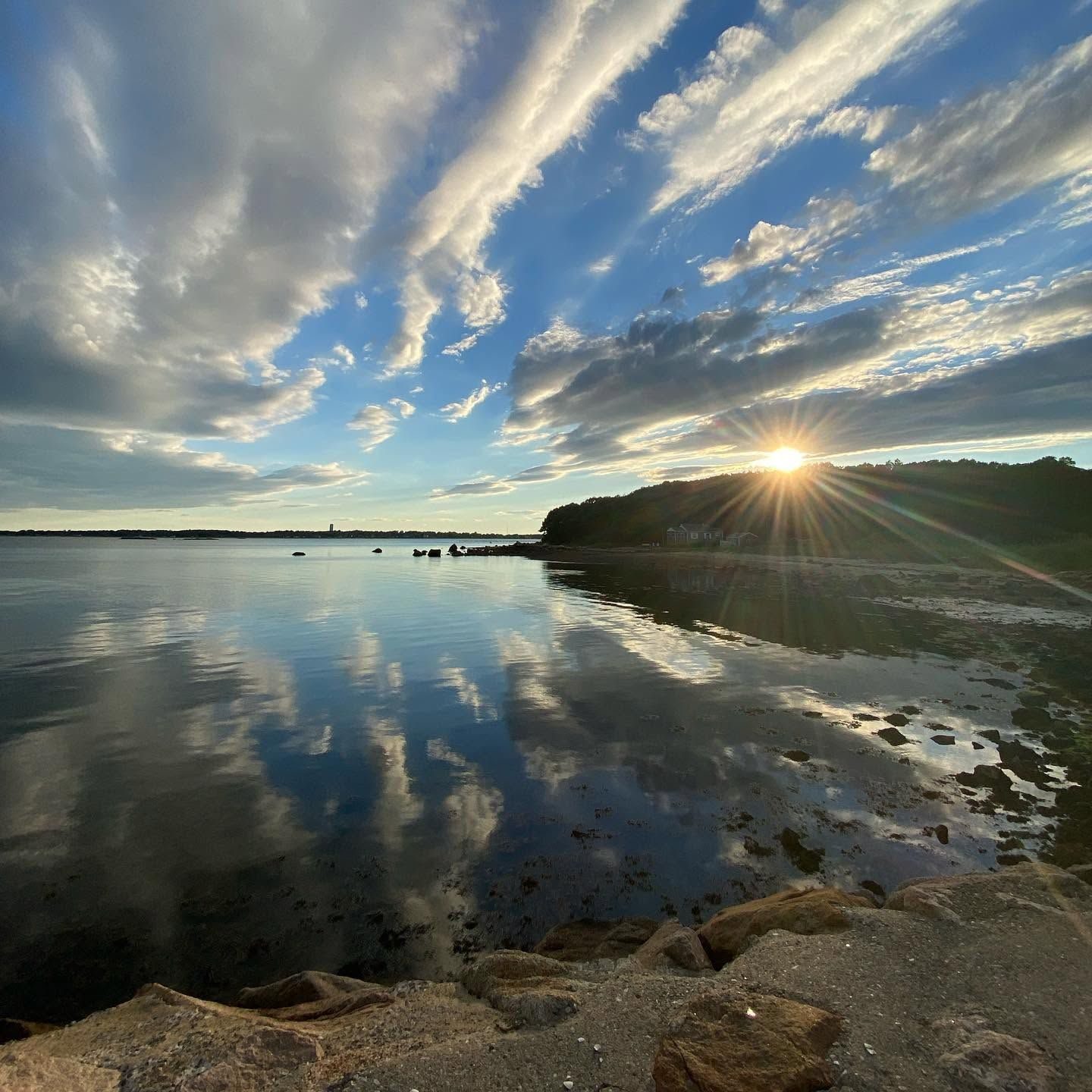 Sunset over calm water and a wooded shore