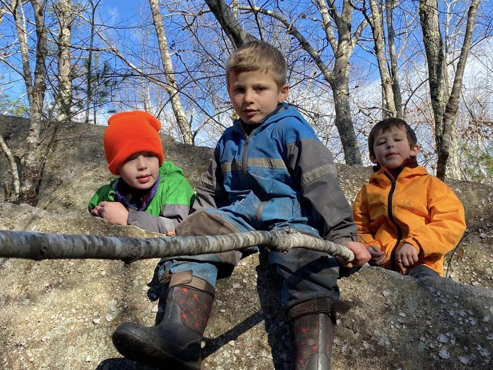 Three kids sitting on a big boulder under blue sky