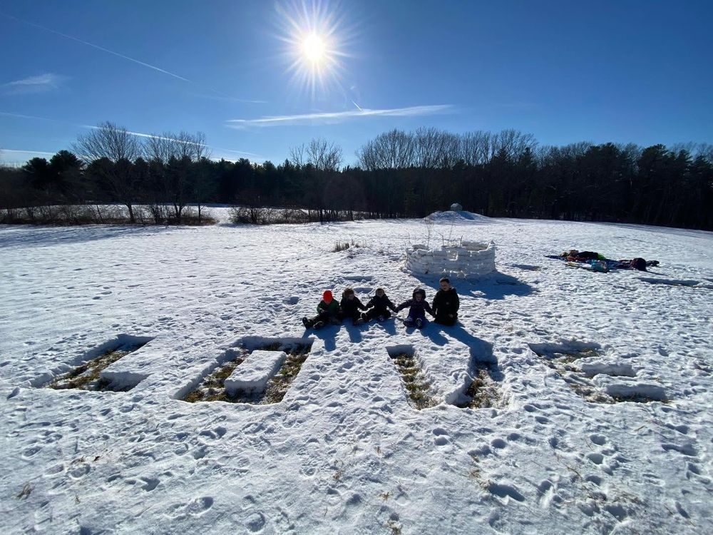 Kids sitting in a sunny snowy field beside a snow fort