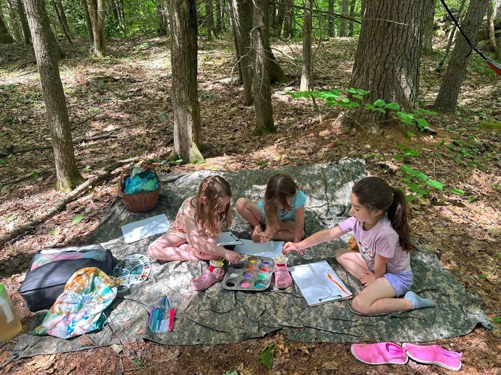 Three girls painting on a tarp in the forest